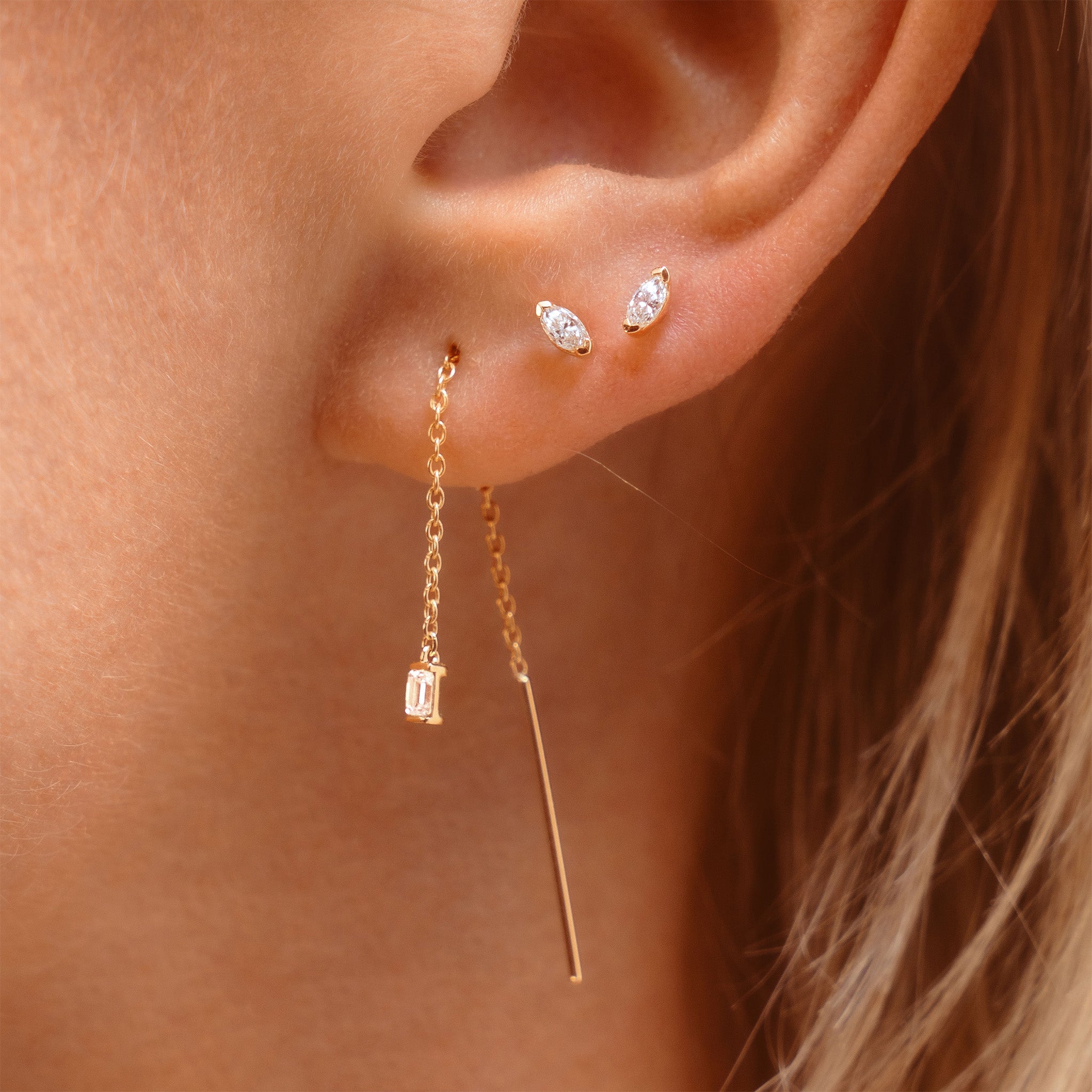 solid gold threader earrings with emerald cut lab diamond and marquise diamond studs on ear
